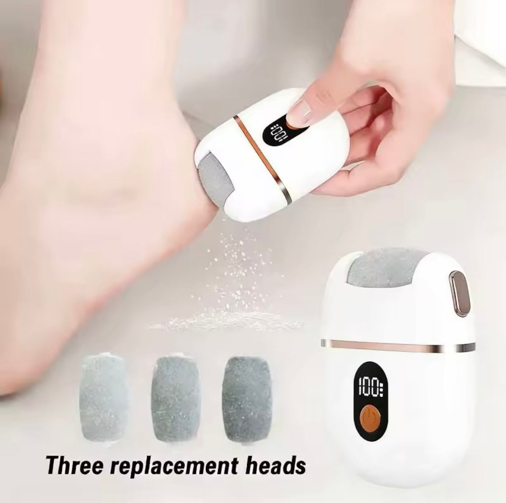A handheld foot care device being used on a person's foot, with three replacement heads shown below and the text 'Three replacement heads.' The main product is white with a gray abrasive pad and a small metallic accent ring.
